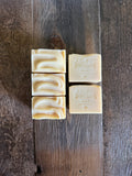 Four bars of handcrafted soap arranged on a rustic dark wood background. Two bars on the left are stacked horizontally to show a swirled marbled texture, and two bars on the right are stacked vertically showing the embossed brand name 'Wild River Soaps'.