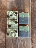 Black and green soaps with hemlock cones and rosemary on top.