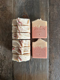 Image shows a group of pink and tan colored soaps with rose petals on top.