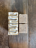 Six bars of handmade soap arranged on a rustic dark wood background, with four bars stacked vertically on the left in a swirled pattern and two bars standing upright on the right embossed with the brand name 'Wild Rivers Soaps'.