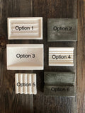 Photo shows a variety of limestone soap dishes in white and grey colors. Option 1 has three ridges in the middle. Option 2 is a flat rectangle. Option 3 is large with ridges on two sides. Option 4 is small with lots of little ridges in the middle. Option 5 is small with 5 ridges all the way across. Option 6 is medium size with one large groove in the middle.